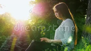 年轻漂亮的女商人在笔记本电脑上打字，<strong>坐在</strong>靠近树的草地上，女人在<strong>公园里</strong>用笔记本